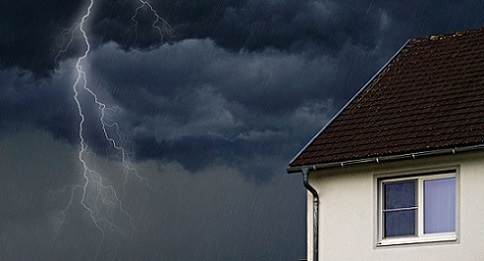 Ein Blitz neben einem weißen Haus mit braunen Dachziegeln.