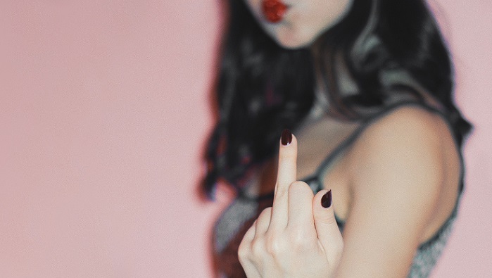 Junge Frau mit schwarzen Haaren zeigt ihren Mittelfinger in die Kamera.