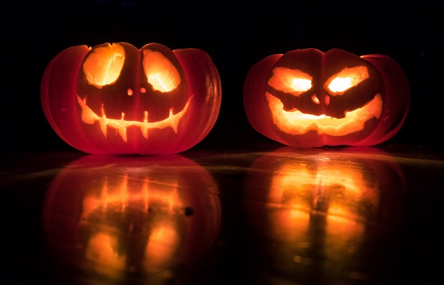 Zwei brennende Kürbisse mit eingeritzten Grimassen spiegeln sich auf einem Tisch.