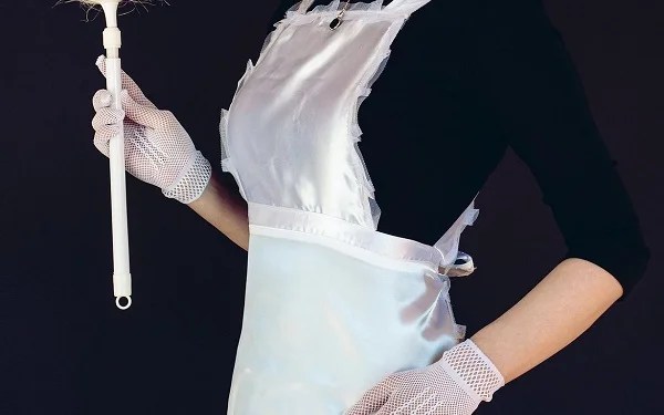 Hausmädchen mit weißer Schürze, weißen Handschuhen und schwarzem Outfit hält einen Staubwedel in der Hand.